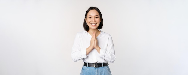 Retrato de menina asiática feliz rindo e sorrindo mostrando obrigado gesto namaste grato por smth de pé sobre fundo branco