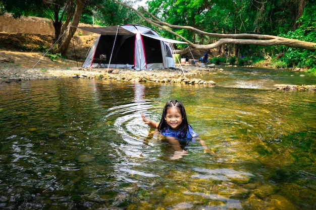 Retrato de menina asiática jogando água da natureza perto da barraca ao ir acampar no parque natural