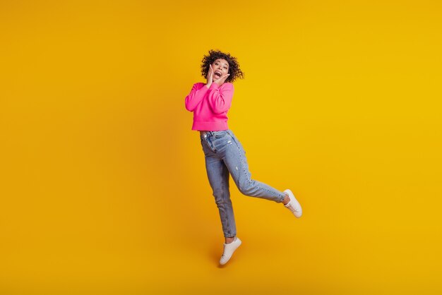 Retrato de menina ativa e positiva pulando, se divertindo no fim de semana livre, isolado no fundo amarelo