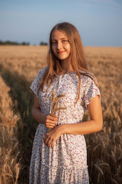 Retrato de menina bonita com um buquê de espigas. Garota de vestido branco no campo de centeio