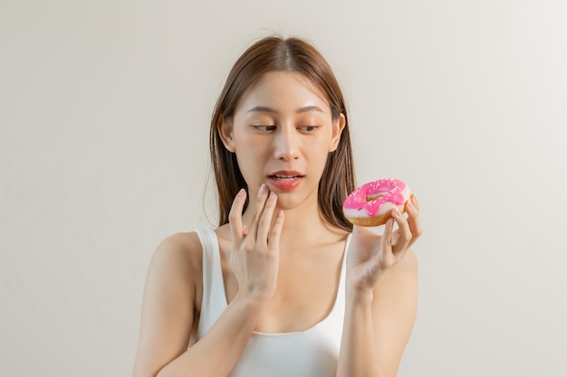 Retrato de menina bonita e atraente, jovem adolescente asiática segurando a emoção de rosquinha rosa rosquinha desfrutar de dieta doce Dieta para perda de peso para emagrecer Espaço de cópia de fundo branco isolado
