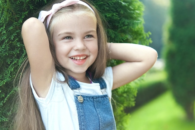 Retrato de menina bonita em pé ao ar livre no parque de verão, sorrindo alegremente.