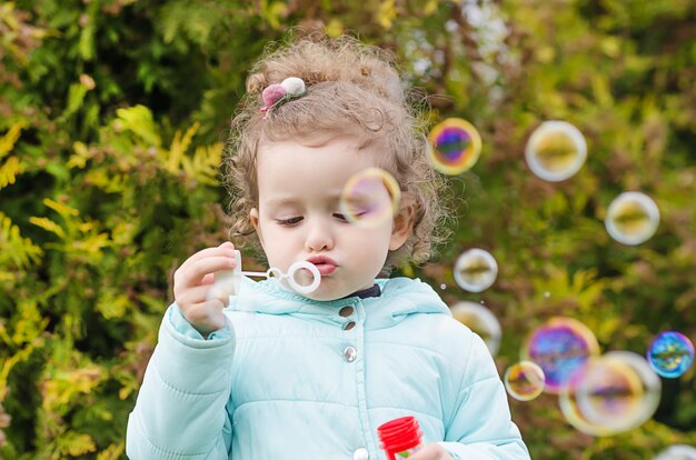 Retrato de menina bonita feliz soprando bolhas de sabão na natura. lazer infantil. jogos ao ar livre engraçados