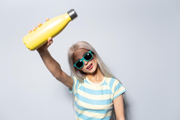 Retrato de menina bonita segurando a garrafa de água térmica amarela no fundo branco