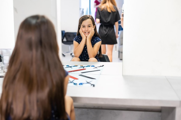 Retrato de menina bonita sentada à mesa com acessórios em um salão de cabeleireiro