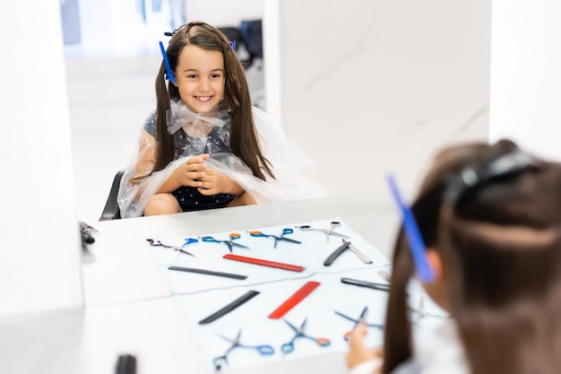 Retrato de menina bonita sentada à mesa com acessórios em um salão de cabeleireiro