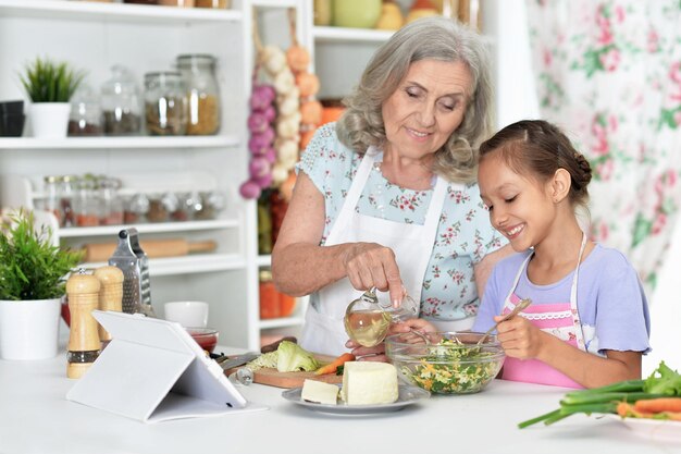 Retrato de menina bonitinha com a avó cozinhando juntos na mesa da cozinha