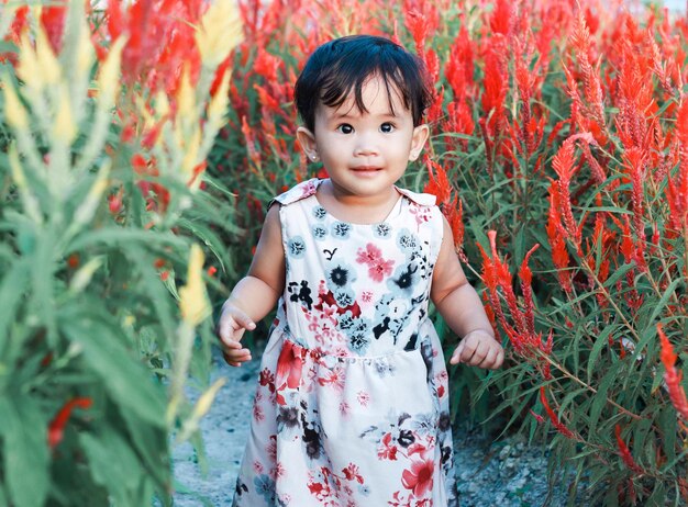 Retrato de menina bonitinha, feliz e sorridente de dois anos brincando no jardim de flores