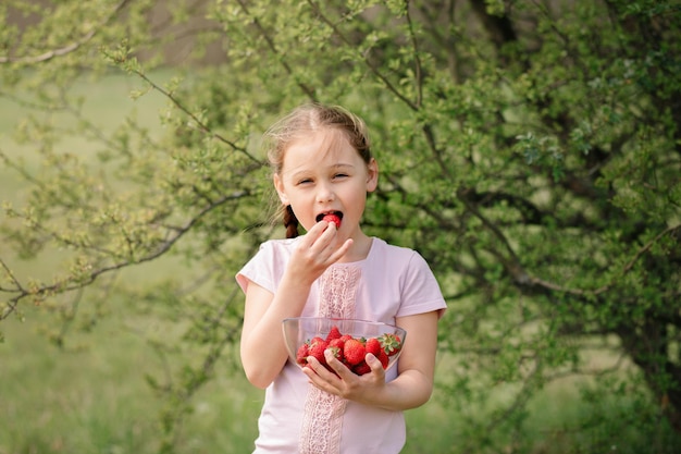 Retrato de menina bonitinha feliz está comendo morangos no dia de verão Foco suave