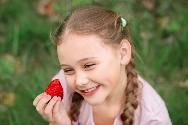 Retrato de menina bonitinha feliz está comendo morangos no dia de verão Foco suave