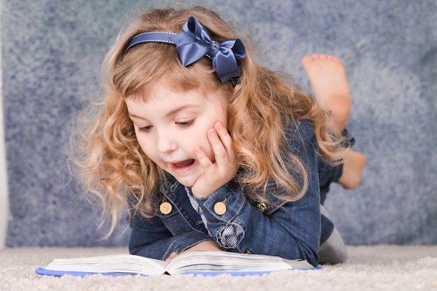 Retrato de menina bonitinha lendo livro enquanto estava deitado no chão