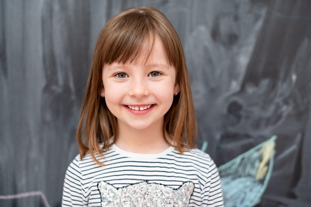 retrato de menina bonitinha sorridente feliz em pé na frente do quadro negro