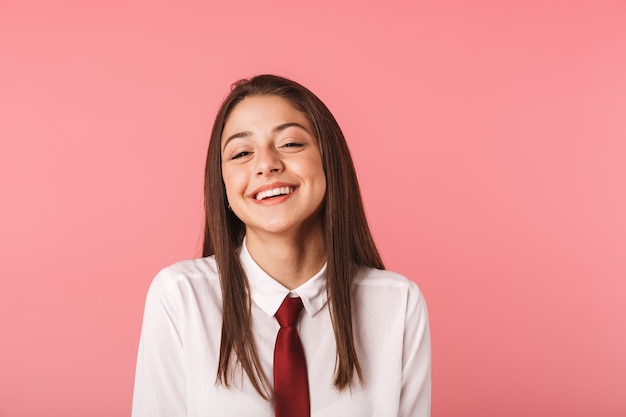 Retrato de menina caucasiana de 15 a 16 anos em uniforme escolar em pé, isolado sobre uma parede vermelha