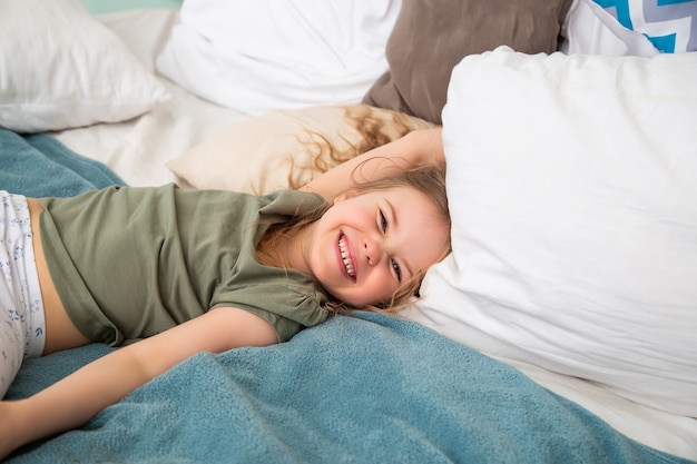 retrato de menina caucasiana deitada na cama e brincando sorrindo olhando para a câmera