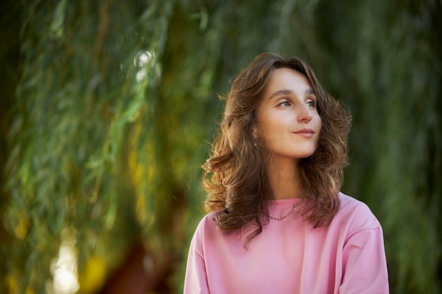 retrato de menina caucasiana em uma camiseta rosa no parque garota feliz sorri e olha para a câmera