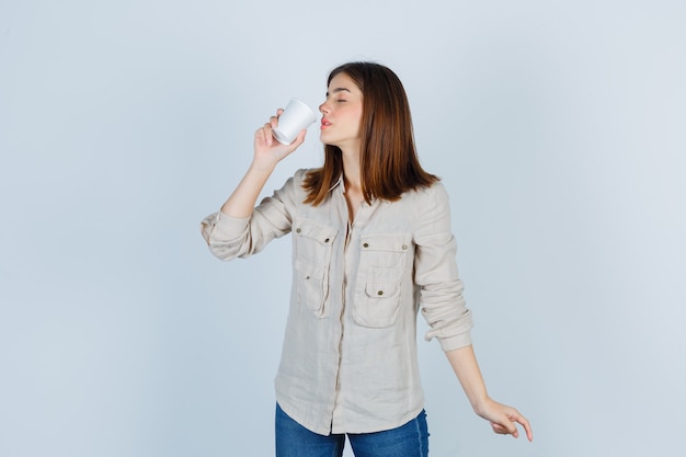 Retrato de menina cheirando café em copo plástico em camisa e parecendo encantado