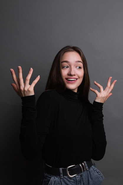 Retrato de menina chocada na camisa preta sobre fundo cinzento escuro. Jovem surpreendida