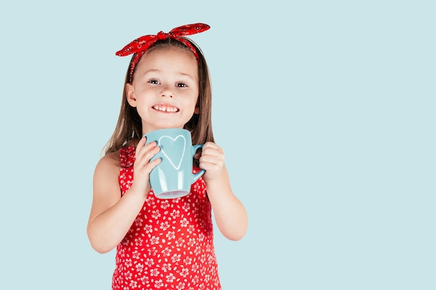 Retrato de menina com cabelo comprido segurar na caneca azul de mãos com coração sorrindo isolado sobre fundo azul. Parabéns pelo dia dos namorados, aniversário, conceito de dia das mães. Copie o espaço.