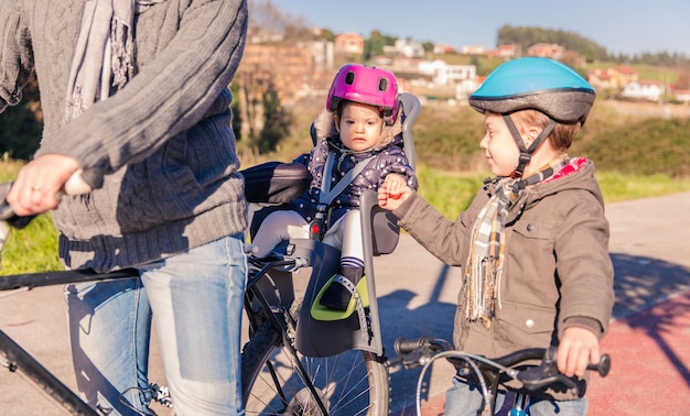 Retrato de menina com capacete de segurança na cabeça, sentado no assento da bicicleta e apertando a mão de seu irmão. conceito de segurança e proteção infantil.