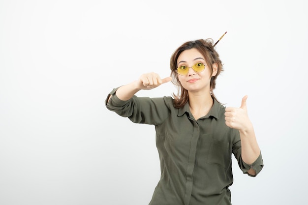 Retrato de menina com coque bagunçado em copos de pé e dando polegares para cima. foto de alta qualidade