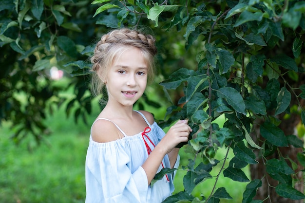 retrato de menina com rabo de cavalo na cabeça fica na folhagem verde na criança do jardim na fazenda