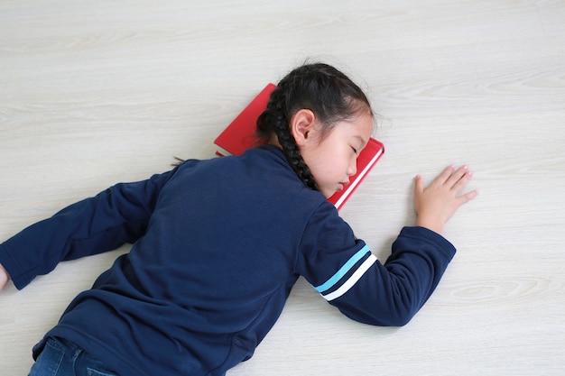 Retrato de menina criança asiática dormindo sobre um livro sobre piso laminado de madeira