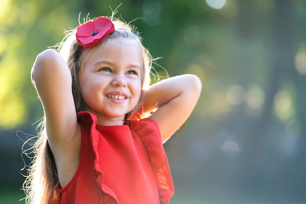 Retrato de menina criança bonita feliz no vestido vermelho, sorrindo ao ar livre, aproveitando o dia quente de verão ensolarado.