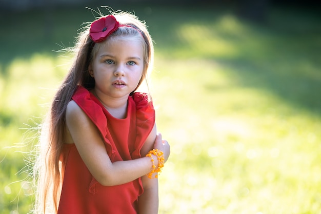 Retrato de menina criança muito elegante com vestido vermelho, aproveitando o dia quente de verão ensolarado.