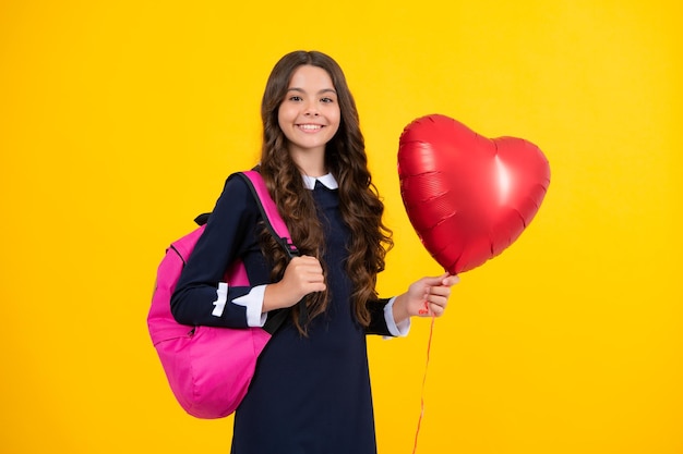 Retrato de menina da escola adolescente com bolsa escolar segura balão de coração isolado em fundo amarelo Eu amo a escola Eu amo a escola