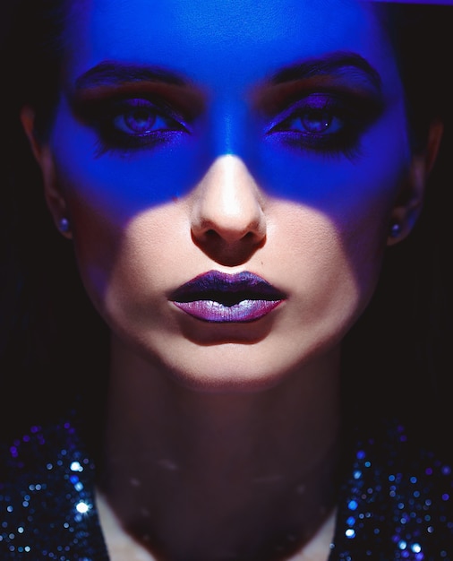 Retrato de menina da moda com maquiagem elegante e luz de néon azul no rosto em um fundo preto no estúdio