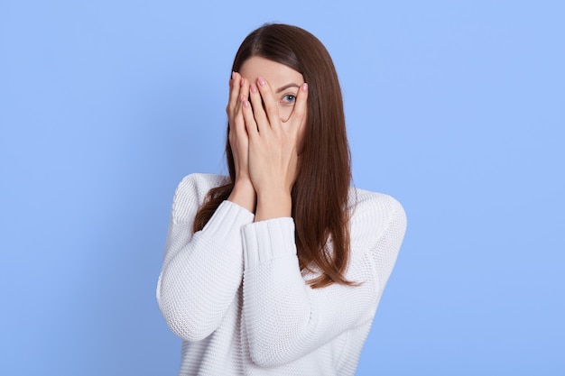 Retrato de menina de cabelos escuros escondendo os olhos enquanto se sente envergonhado