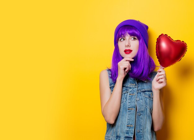 Retrato de menina de estilo jovem hippie com cabelo roxo e balão de forma de coração em fundo amarelo. feriado de são valentim