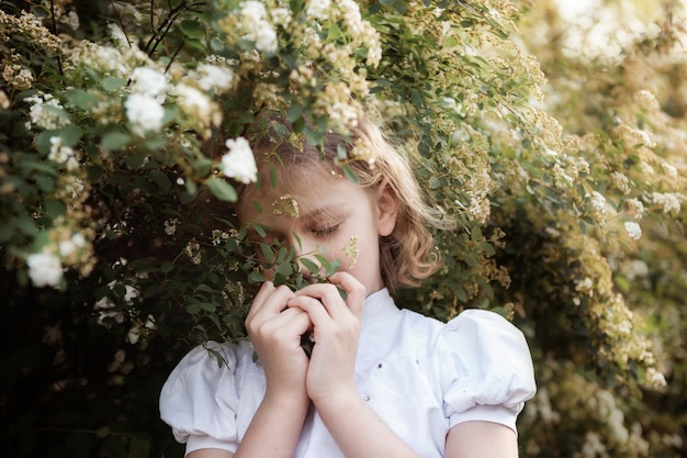 Retrato de menina doce com longos cabelos loiros, close-up, arbusto de floração. conceito de tempo de primavera.