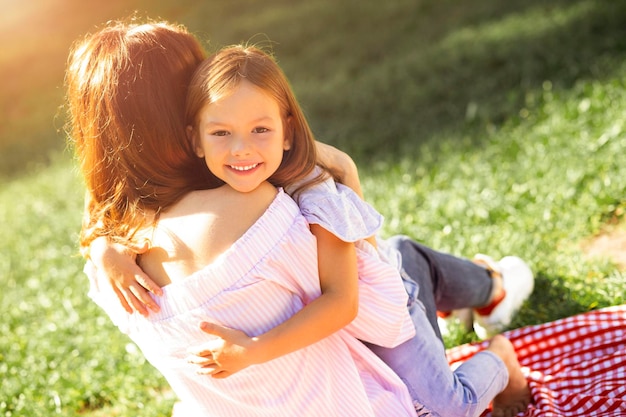 Retrato de menina feliz, abraçando a mãe e olhando para a câmera no parque