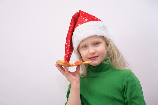 Retrato de menina feliz com chapéu de Papai Noel comendo pizza no fundo branco