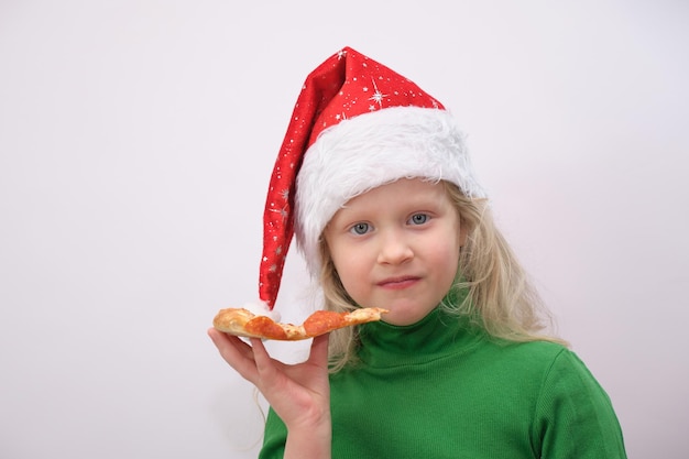 Retrato de menina feliz com chapéu de Papai Noel comendo pizza no fundo branco