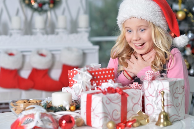 Retrato de menina feliz com chapéu de Papai Noel sentada com presentes de Natal