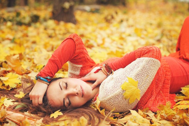 Retrato de menina feliz descansando, deitada no outono maple folhas no parque, olhos fechados, vestido com um suéter da moda