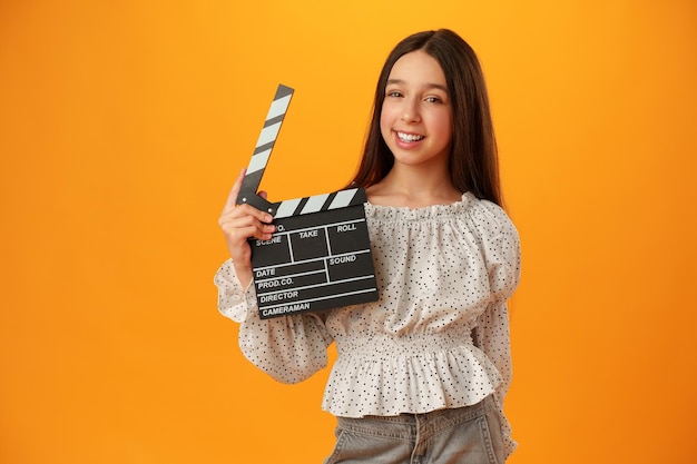 Retrato de menina feliz e sorridente segurando claquete em fundo amarelo
