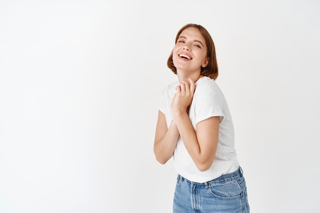 Retrato de menina feliz natural, rindo e sorrindo, segurando as mãos pressionadas contra o peito. linda senhora expressa emoções positivas