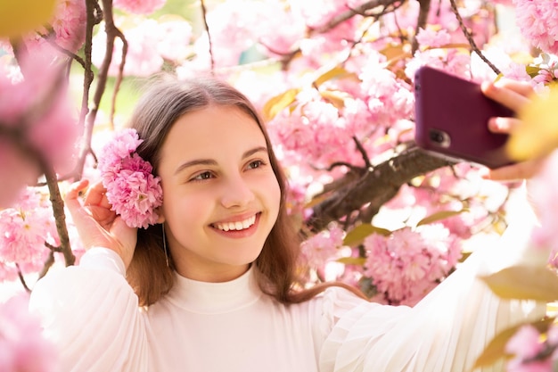 Retrato de menina feliz tomando selfie na árvore de floração sakura na primavera.