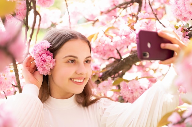 Retrato de menina feliz tomando selfie na árvore de floração sakura na primavera.