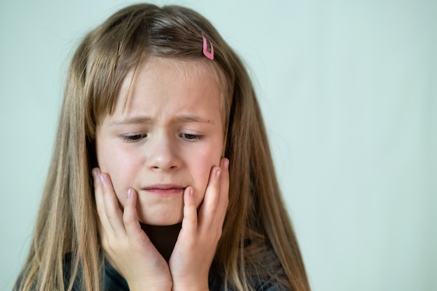 Foto retrato de menina infeliz cobrindo o rosto com as mãos a chorar.