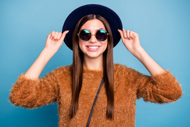 Retrato de menina jovem com conteúdo sincero se divertindo, jornada de férias de inverno, toque em um chapéu elegante, use roupas bonitas isoladas sobre a parede azul