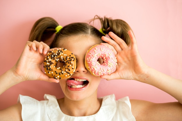 Retrato, de, menina jovem, olhando, dois, cor-de-rosa, donuts, cor-de-rosa, fundo