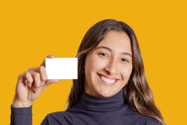 Retrato de menina latina sorridente mostrando um cartão em branco isolado em fundo amarelo