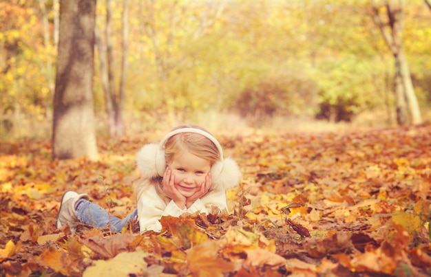 Retrato de menina loira deitada no outono amarelo maple folhas estendidas as mãos e sorrindo.