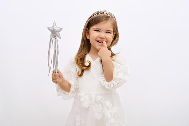 Retrato de menina loira sorridente princesa conto de fadas fada com varinha mágica na mão e coroa na cabeça no vestido branco no fundo branco desejo cumprimento sonhos de infância cópia espaço