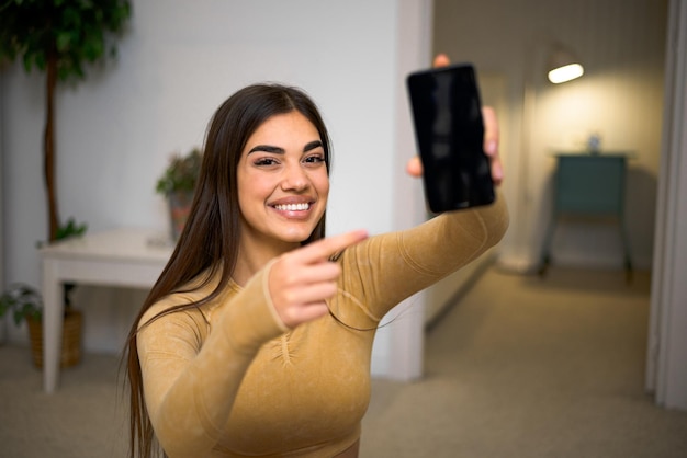 Retrato de menina morena alegre apontando para o telefone sorrindo