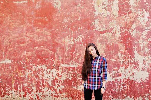 Retrato de menina morena jovem bonito na camisa xadrez na superfície da parede vermelha grunge. Copie espaço, espaço para texto